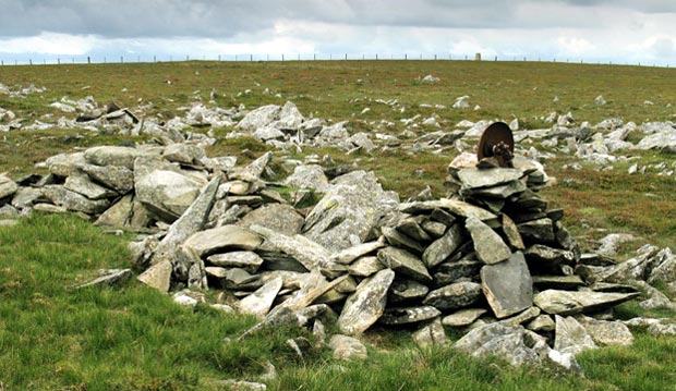 Large stone slabs east of the top of Pykestone Knowe with the trig point in view.