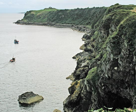 View back to Cruggleton Castle from Sliddery Point with two fishing boats